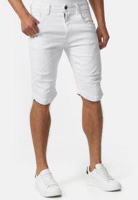 Short en jean blanc à coupe ajustée, doté de cinq poches, de détails cousus et d'une fermeture éclair. Porté avec des baskets blanches.