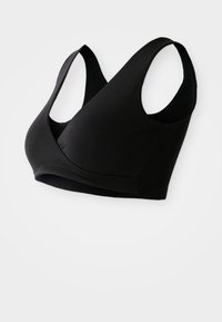 Melnā bezvadu sporta krūšturis ar V-veida dizainu, plašām siksnām un gludu tekstūru, ar bezšuvju apdari un bez redzamām detaļām.