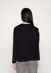 Blusa nera a maniche lunghe con scollatura rotonda e spacchi laterali, dotata di chiusura con zip sul retro. Texture liscia, design semplice.