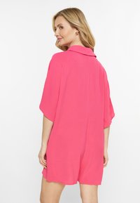 Rosa jumpsuit med krage, tillverkat av textil med struktur, med korta ärmar och en avslappnad passform, med en slät finish och lätt drapering.