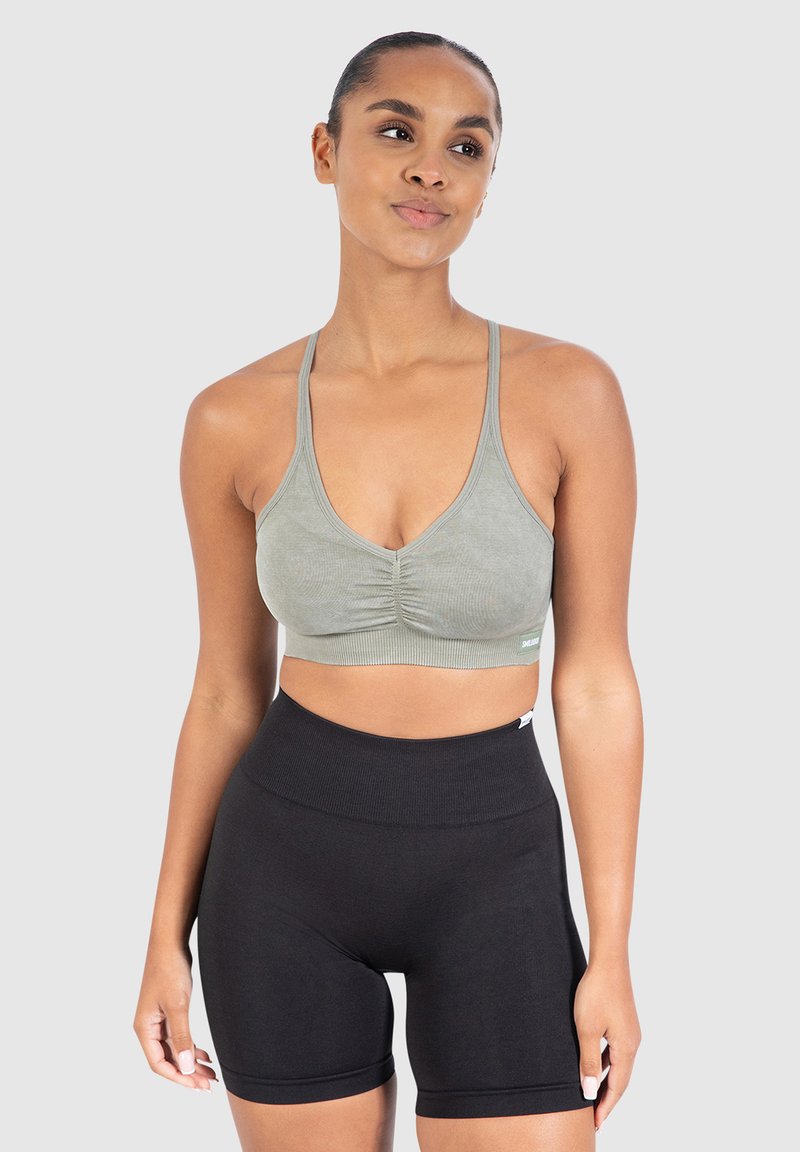 Vaaleanvihreä ribatty urheilbra, jossa on rypytetty yksityiskohta, yhdistettynä korkea vyötäröön mustiin shortseihin, jotka on valmistettu pehmeästä, joustavasta kankaasta. Yksinkertainen muotoilu.