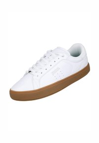 Zapatillas deportivas blancas con parte superior de cuero liso, detalles perforados y suela de goma marrón. Presentan un diseño de cordones y un acento de logo.