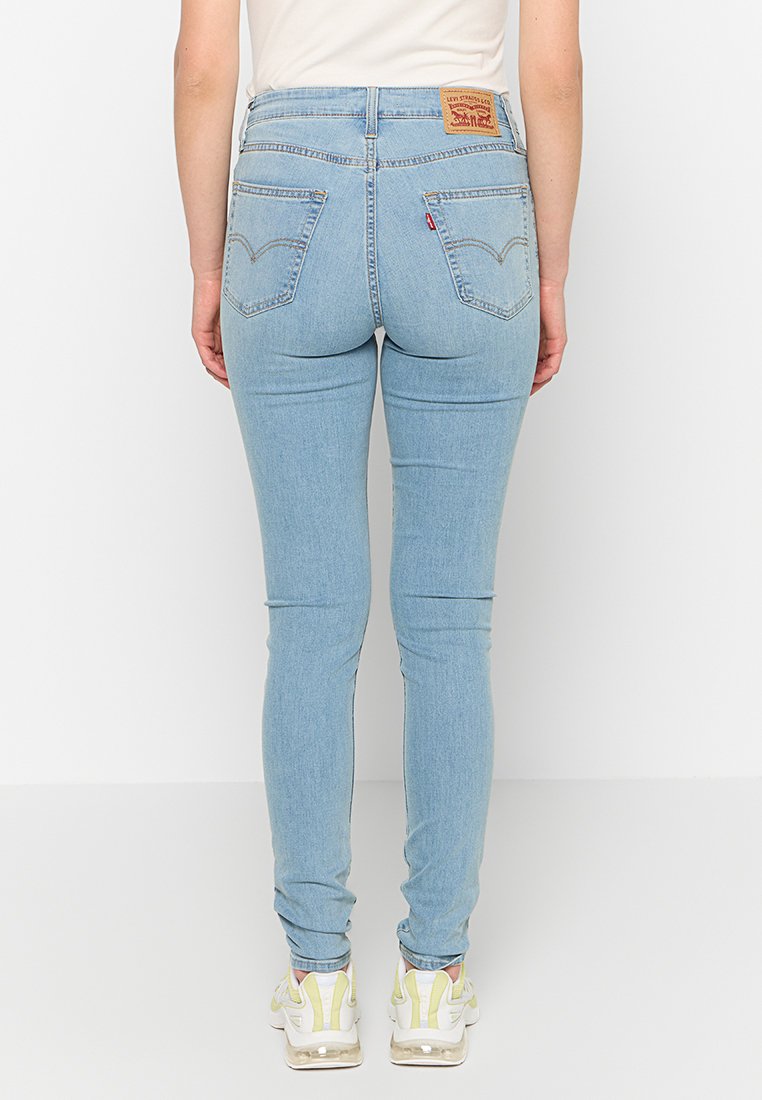 Vaqueros skinny de mezclilla azul claro con cintura alta, con un parche de marca de cuero en la parte posterior y dos bolsillos a cada lado.