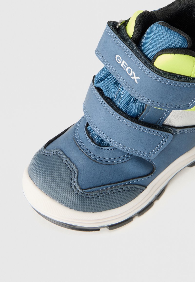 Baskets pour enfants bleu et vert néon avec des sangles Velcro et un marquage "GEOX" sur un fond blanc.