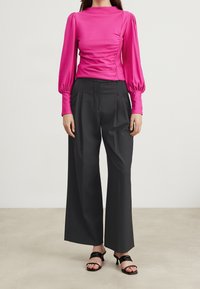 Figurpassad rosa blus med puffärmar och rynkdetalj; kombinerad med vida svarta byxor och svarta remsandaler.