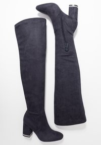 Lårhöga, mörkgrå mockastövlar med en kraftig klack. Har en sidodragkedja och en texturerad finish. Klacken har en metallisk detalj vid basen.