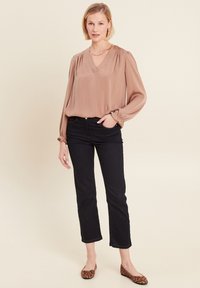 Blusa ampia color taupe con scollatura a V e dettagli arricciati sulle spalle, abbinata a jeans dritti scuri e ballerine con stampa leopardata.