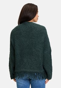 Dunkelgrüner, strukturierter Pullover mit lockerer Passform, fransigem Saum und langen Ärmeln. Weiches, gemütliches Material mit einem samtigen Finish.