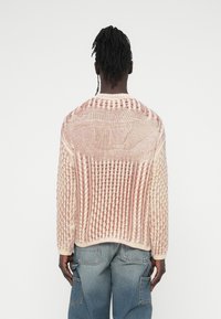 Pull en maille aux tons crème et rose, présentant un motif texturé avec des sections en maille ajourée. Encolure ronde et poignets côtelés aux manches.