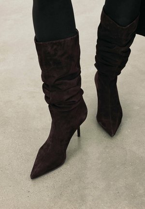 Brune ruskind ankelstøvler med spids tå og højt stiletto-hæl, med detaljeret rynkning omkring lægområdet.