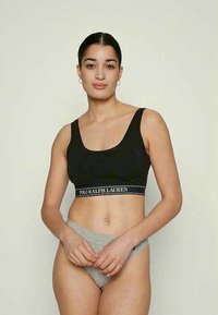 Μαύρο βαμβακερό crop top με φαρδιές τιράντες και λογότυπο. Συνδυασμένο με γκρι εσώρουχα χαμηλής μέσης, που δείχνουν λεία υφή και εφαρμοστό σχέδιο.