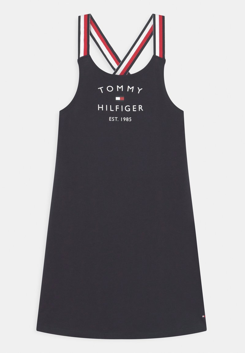 Granatowa sukienka bez rękawów z krzyżującymi się czerwonymi, białymi i czarnymi paskami oraz tekstem i logo „Tommy Hilfiger Est. 1985” na przodzie.