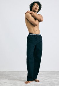 Fekete, laza szabású nadrág széles derékpánttal, amelyen fehér színnel a "BJÖRN BORG" felirat szerepel. Az anyaga sima, enyhe fényével.