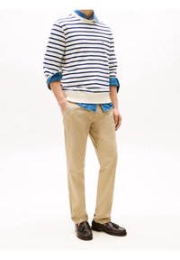 Weißer und marineblauer gestreifter Pullover, darüber ein hellblaues Hemd getragen, kombiniert mit beigefarbenen Chinos und dunklen Loafers. Klassischer, lässiger Stil.