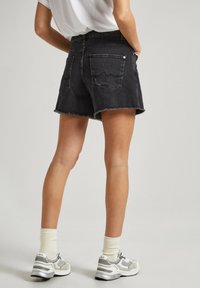 Shorts de mezclilla negra con dobladillo deshilachado, diseño de cinco bolsillos y detalles de costura sutiles. Combinados con calcetines y zapatos deportivos de color claro.