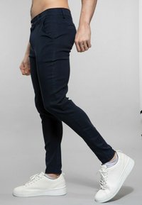 Pantalons slim-fit bleu marine en tissu satiné, avec poches latérales et un design à l'avant plat, associés à des baskets blanches.