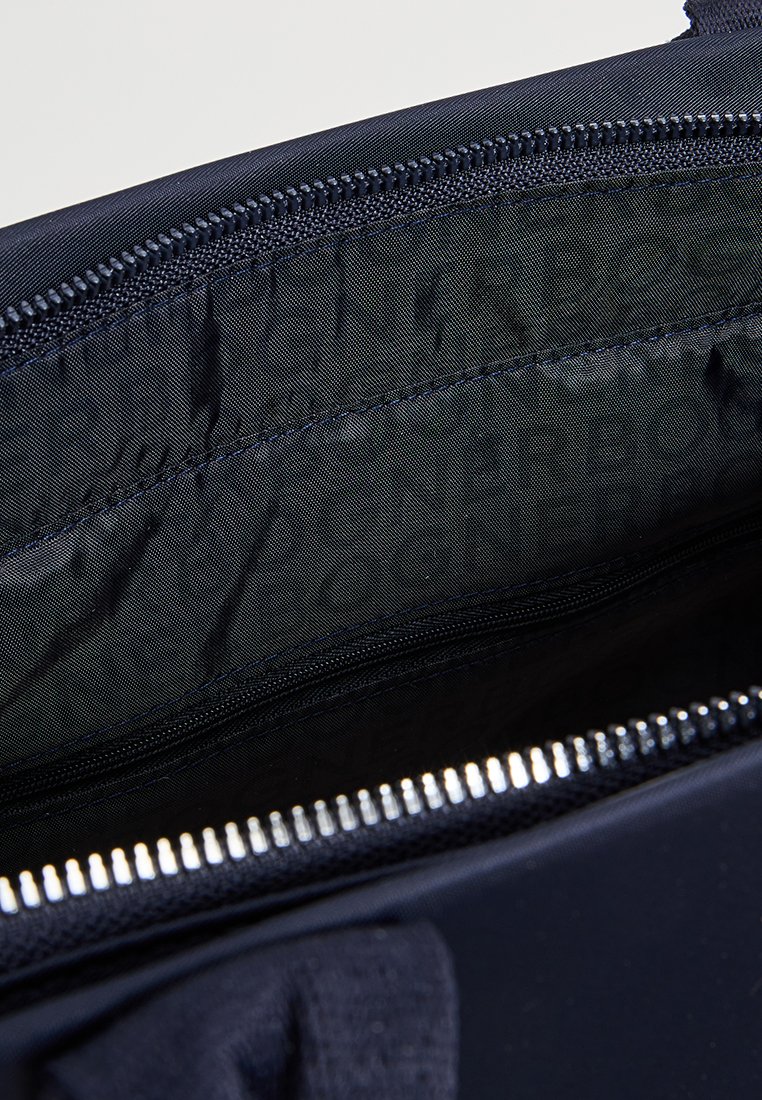 Innenseite einer marineblauen Stofftasche mit glattem Futter, ausgestattet mit einem Reißverschluss und einer dezenten Markenprägung im Inneren.