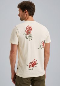 T-shirt en coton couleur crème ornée d'imprimés botaniques rouges et verts au dos. Manches courtes et coupe décontractée.