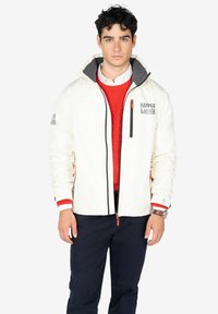 Chaqueta impermeable blanca con cuello gris, cremallera negra y detalles en naranja. Presenta un logo en el lado izquierdo del pecho y bolsillos en las mangas.