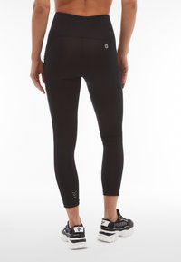 Leggings sportivi neri con vita alta, texture liscia e dettagli riflettenti sulla parte inferiore della gamba. Abbinati a sneakers nere.