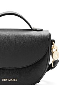 Zwarte lederen handtas met een afgeronde klep, textuur oppervlak, gouden hardware en een afneembare schouderband. Merkm naam "HEY MARLY" in reliëf op de voorkant.
