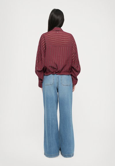 Burgundy striped blouse with a relaxed fit and gathered hem, paired with light blue wide-leg jeans. Cotton with a textured finish.