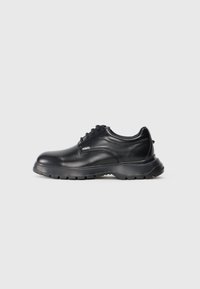 Chaussure noire en cuir avec un bout arrondi, design à lacets et semelle en caoutchouc texturée. Présente un logo "KARL" sur le côté. Finition lisse.
