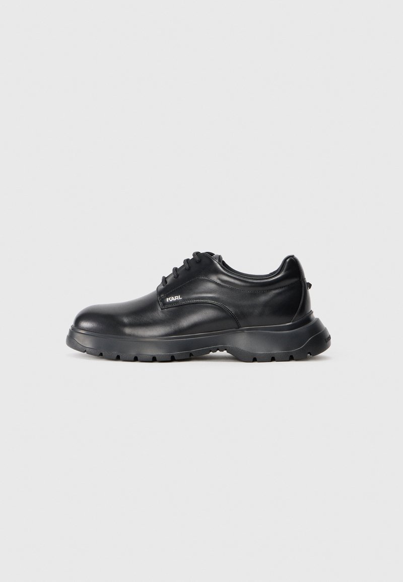 Chaussure noire en cuir avec un bout arrondi, design à lacets et semelle en caoutchouc texturée. Présente un logo "KARL" sur le côté. Finition lisse.