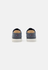 Denimist sneakerid, millel on tekstureeritud tumesinine ülemine osa, pruuni aktsentidega kand ja valge kummist tald; küljele on lisatud väike logo. 
