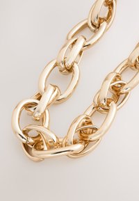 Gold metal chain necklace featuring interlocking oval and round links with a polished finish, highlighting smooth texture and reflective surface.
