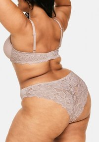 BH mit Spitzenrücken und passendem Panty-Set in Hellbeige. Der BH verfügt über verstellbare Träger und florale Spitzenakzente; der Panty hat ähnliche Spitzenverzierungen.