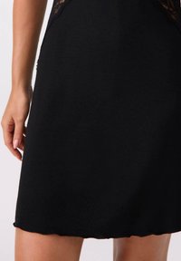 Czarna sukienka o dopasowanym kroju. Posiada koronkowe detale wzdłuż dekoltu, miękką fakturę tkaniny oraz falbaniasty dół.