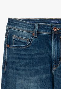 Jeans in denim blu scuro con cuciture arancioni, una piccola tasca frontale e un passante per la cintura. L'etichetta del marchio è visibile all'interno della vita.