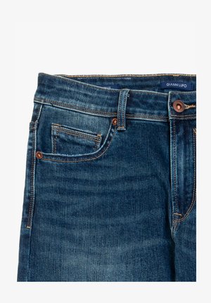 Donkerblauwe denim jeans met oranje stiksels, een klein voorvak en een riemlus. Het merklabel is zichtbaar aan de binnenkant van de tailleband.