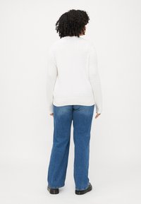 Hvit textured genser med lange ermer og rund hals, sammen med blå vide jeans og svarte platåsko.
