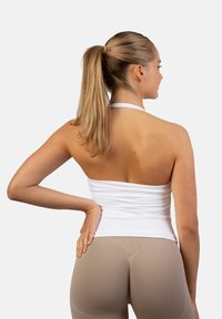 Bela halterneck majica ima prilagojen dizajn z nabranim slogom ob straneh, v kombinaciji z svetlo bež visokim pasom legicami.