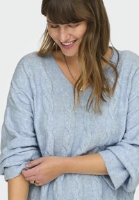 Ljusblå stickad tröja med V-hals och upprullade ärmar. Har ett kabelstickat mönster och en mjuk textur.