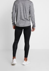 Gray long-sleeve athletic shirt with a textured pattern, paired with black fitted leggings. White athletic shoes complete the outfit.