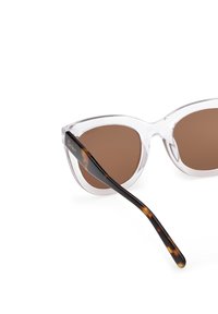 Kattöga solglasögon med genomskinlig plastram och bruna linser, med skalmar i sköldpaddsmönster. Varumärket synligt på sidan.