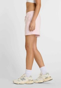 Pantalones cortos de algodón rosa con cintura elástica y cordón; bolsillos laterales. Combinados con zapatillas deportivas gruesas de color claro y calcetines blancos.