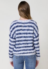 Maglione morbido con righe orizzontali blu e bianche, colletto ampio, spalle scese e polsini a costine. Abbinato a jeans azzurri chiari.