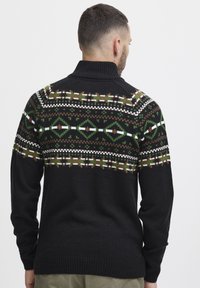 Schwarzer Pullover mit hohem Kragen. Der obere Abschnitt hat ein gemustertes Design in Grün, Braun und Weiß. Strukturierter Strickstoff.