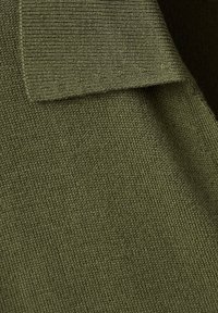 Gros plan d’un tissu tricoté vert olive avec un bord plié mettant en valeur la texture et le motif de couture serré.