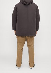 Mörk isolerad jacka med huva, tillsammans med tan cargo byxor. Båda plaggen har enkla designer och praktiska snitt.