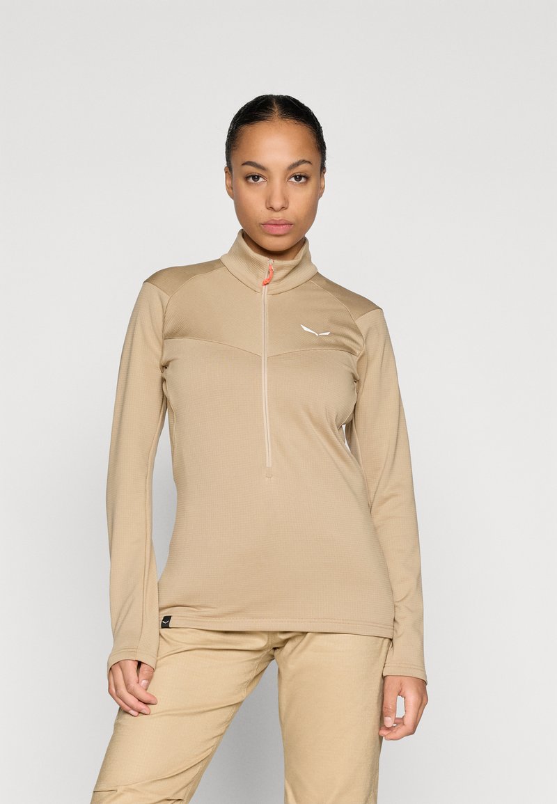 Μπεζ μπλούζα με μακριά μανίκια, ψηλό γιακά και μισό φερμουάρ. Διαθέτει υφασμάτινη υφή και μικρό λευκό λογότυπο στο στήθος.