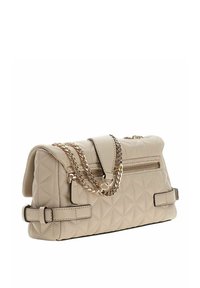 Sac à main matelassé beige avec une bandoulière chaîne, doté d'un rabat supérieur et d'une poche zippée, orné de boucles et d'une texture en cuir lisse.