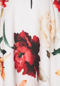 Blommönstrad tyg med stora röda och blekgula blommor på en vit bakgrund med gröna blad, slät textur och lätt design.