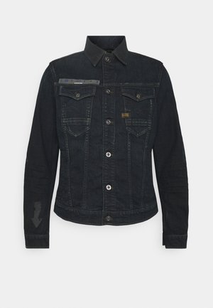 Sort denimjakke med knapper foran, to brystlommer med klap, krave og subtile mærkede patches på brystet og venstre ærme.