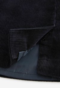 Teflonul de culoare albastru marin are un interior căptușit. Textura prezintă dungi verticale, iar gulerul are margini curate.