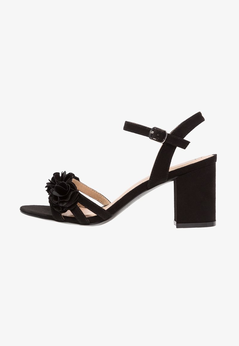 Des sandales à talons en suède noir présentent une accent floral, un design à bout ouvert, une sangle ajustable à la cheville et un talon bloc épais.